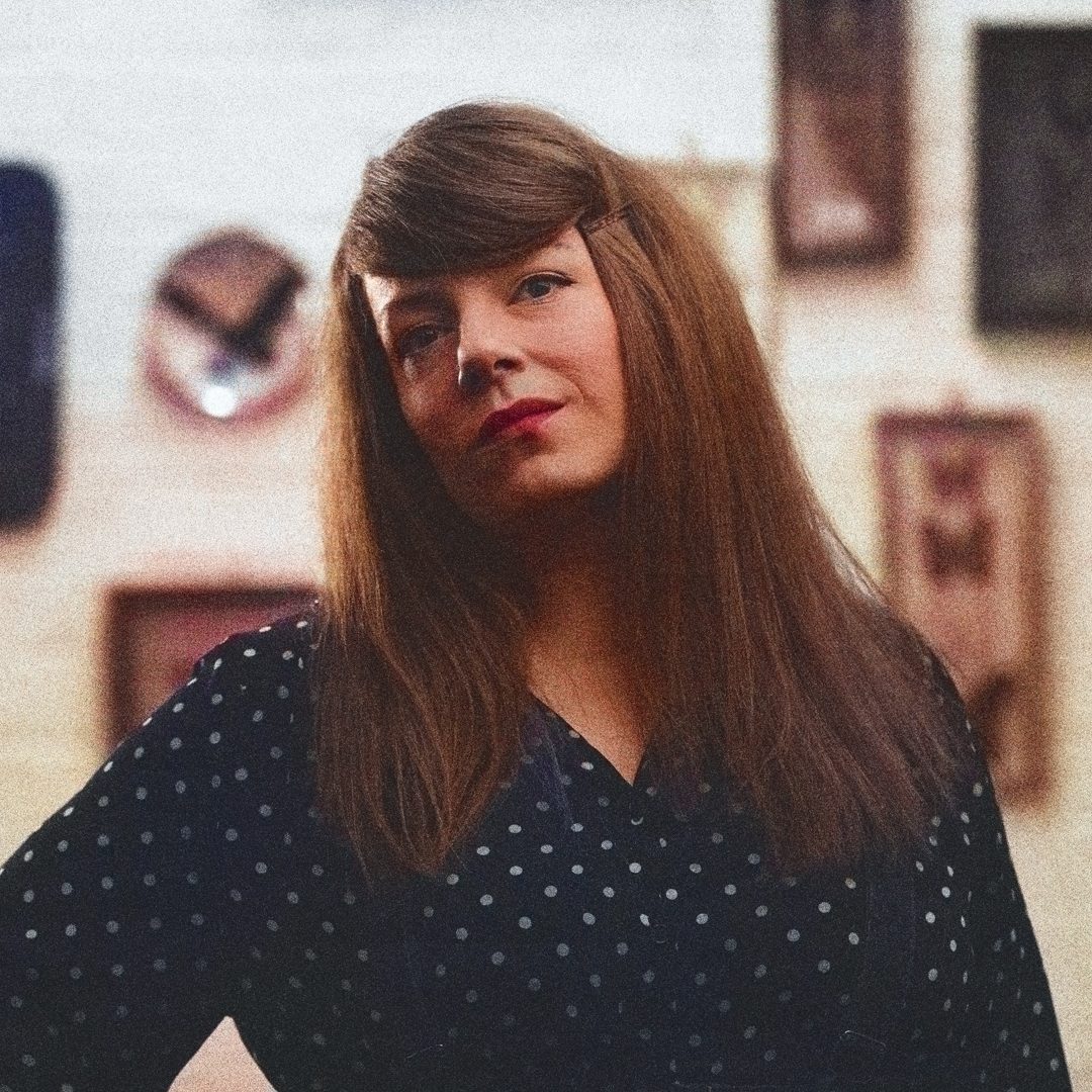 Black and white portrait of Producer Suzanna Holland standing confidently in front of a wall of framed artwork.